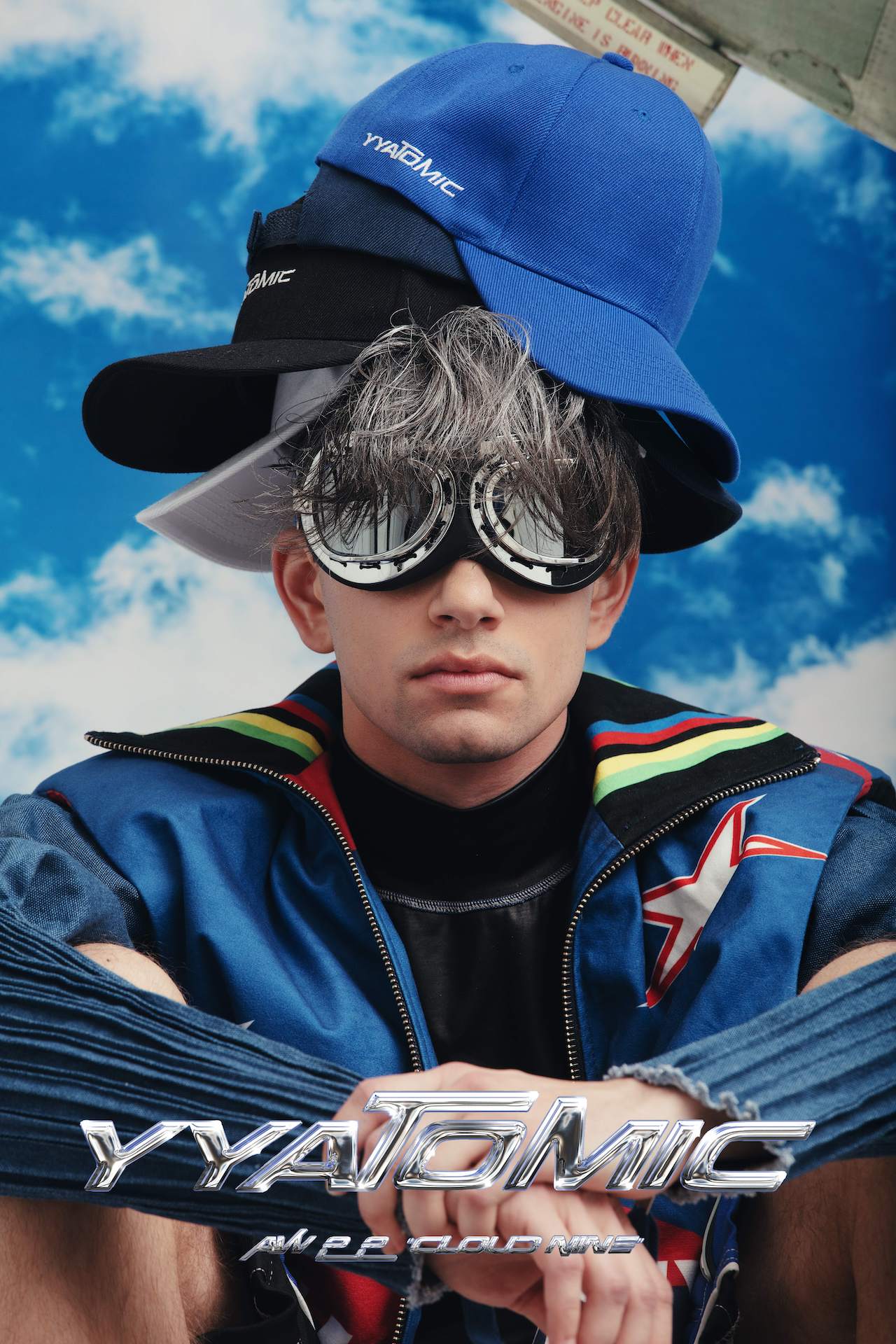 Profile shot of model wearing four YYAtomic snapbacks, aviator goggles, and YYatomic's 2-in-1 Denim Jacket. 