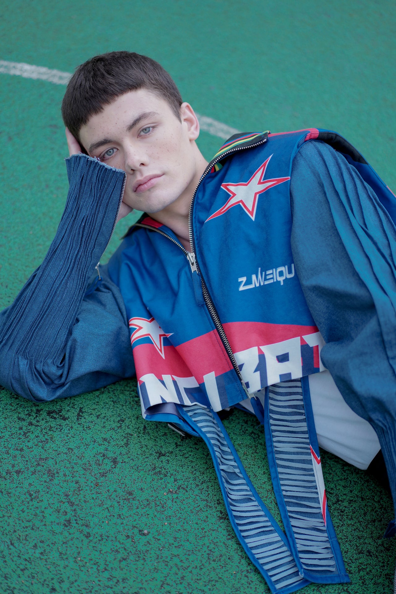 Model wearing YYAtomic 2-in-1 denim jacket laying down on football pitch. 