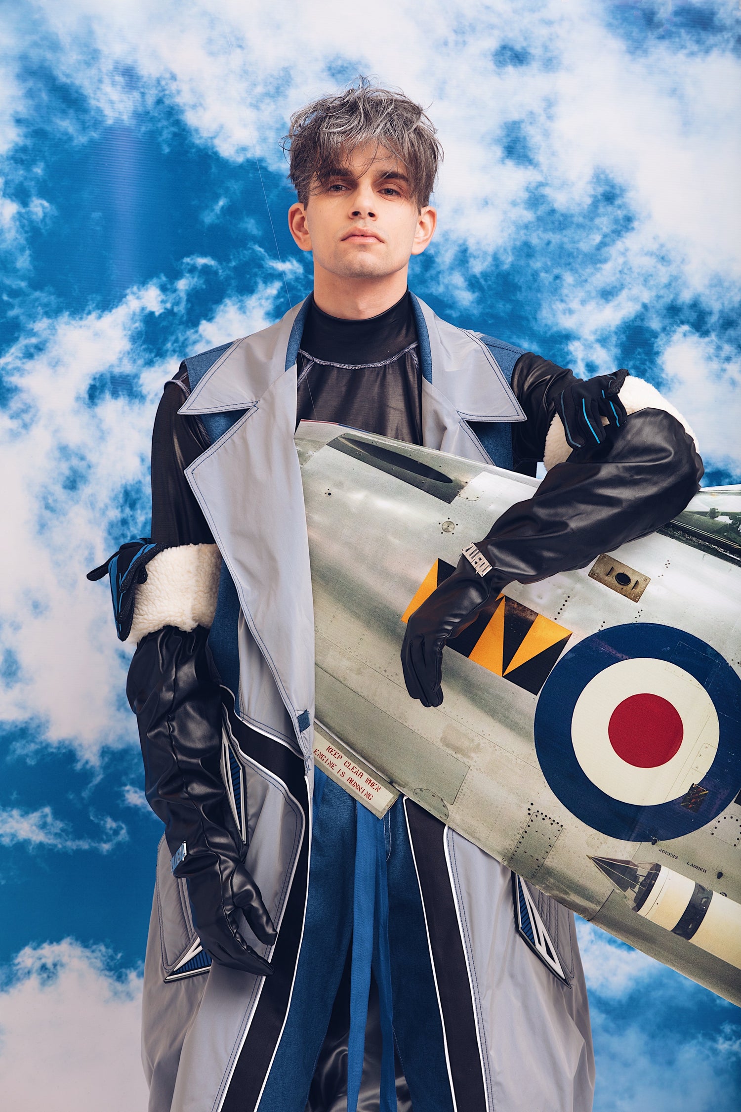 Frontal shot of model wearing YYAtomic Long Patched Waistcoat and holding a cardboard airplane.